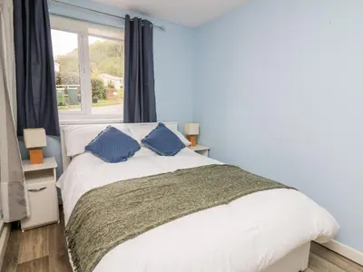 a bedroom with a bed with blue pillows and a window at Cwtsh Cragen in New Quay
