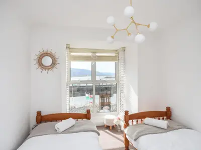 two beds in a white room with a window at Arran House in Barmouth