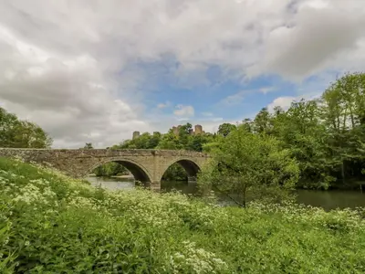 a stone bridge over a river with trees and bushes at 2 The Villa in Ludlow