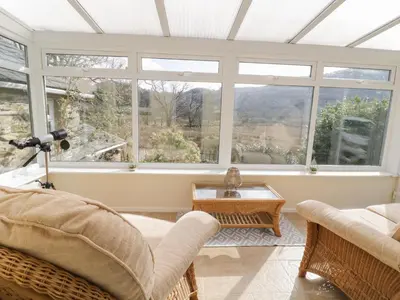 a living room with windows and a couch and a table at The Old Smithy Cottage in Blaenau-Ffestiniog