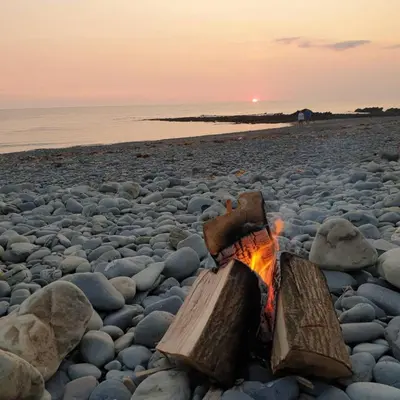 a campfire on a beach with the sunset in the background at Spacious heated Yurt with Hot tub, 5 mins to beach in Bow Street