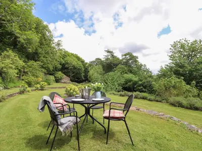 a table and chairs in a garden with trees at Bodowen Coach House in Barmouth