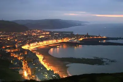 a city with a bridge over a river at night at Bridge View Victorian Townhouse Central Aberystwyth Sleeps 6 in Aberystwyth