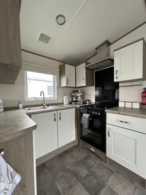 a kitchen with white cabinets and a black stove top oven at Delightful 2 bedroom Caravan, Pencnwc, New Quay in Cross Inn