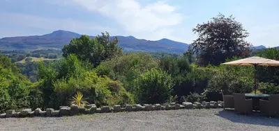 a patio with an umbrella and mountains in the background at Large Mach Apartment at Pen Y Coed Hall in Dolgellau