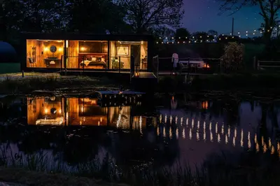 a tiny house sitting next to a pond at night at Rusty Boathouse in Llanarth