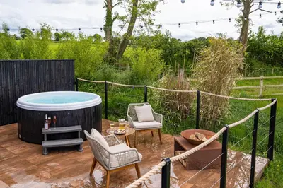 a hot tub on a deck with chairs and a table at Rusty Boathouse in Llanarth