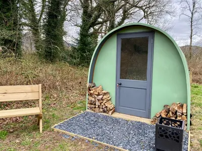 a green dome tent with a pile of fire wood at MotoCamp Wales -Camping Pods in Dolgellau
