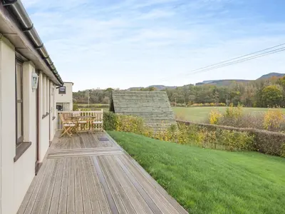 a wooden deck with a table on the side of a house at Beacons Cottage-Uk36406 in Bronllys