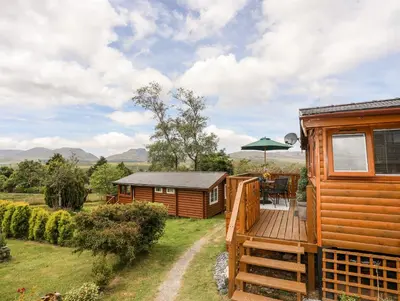 a cabin with a deck and a table and an umbrella at Ty Coed - 63 in Trawsfynydd