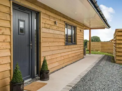 a wooden house with a black door and two plants at Bramley Lodge - Uk38384 in Lyonshall