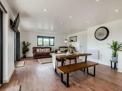 a living room with a table and a clock on the wall at Bramley Lodge - Uk38384 in Lyonshall
