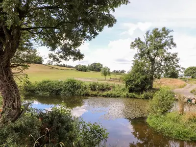 a river with trees and a field in the background at The Moorhen Retreat in Oswestry