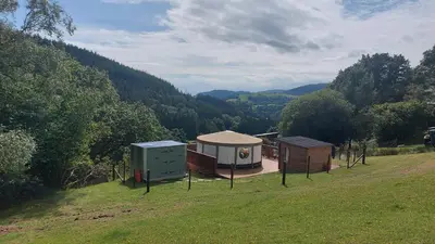 a group of huts in a field with trees at Yurt Uchaf Off-Grid Glamping in Machynlleth