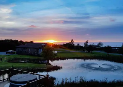 a sunset over a pond in front of a house at Seven Springs in Llanon