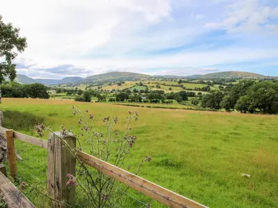 a field with a fence and mountains in the background at The Retreat in Oswestry