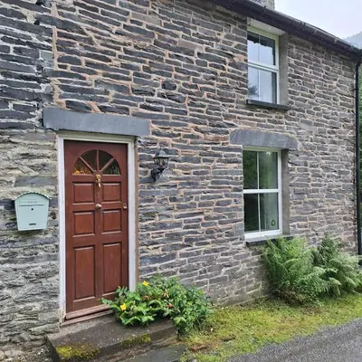 a brick house with a brown door and two windows at Cosy riverside cottage in beautiful Corris in Corris