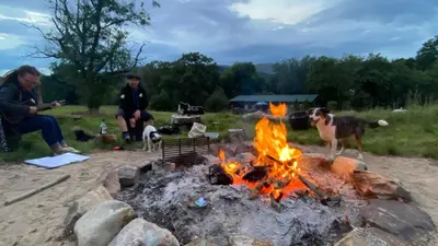 two people and two dogs sitting around a fire at MotoCamp Wales - Lodges in Dolgellau