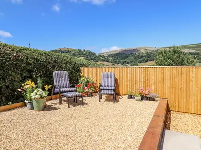 two chairs and flowers on a patio with a fence at Cam O'r Fechan Annexe in Llangollen