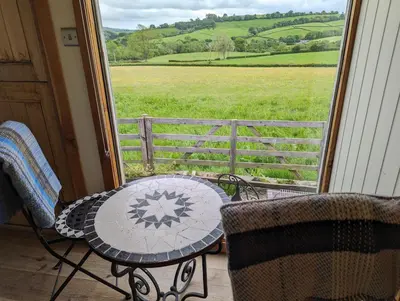 a table and chairs on a porch with a view of a field at Top of the Rock Glamping in Trefeglwys