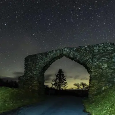 a stone archway under a night sky with a tree at Forester's Retreat Glamping - Dinas View - Vaccinated dogs over the age of 2 are accepted in Aberystwyth
