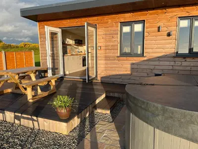 a wooden cabin with a deck with a table and a bench at MAESLLAN CABINS 'Hud Y Machlud' in Cross Inn