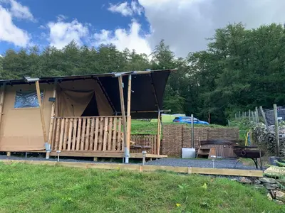a tent with a table and a grill in a field at Mountain View Safari Tent with Hot Tub in The Heart of Snowdonia in Dolgellau