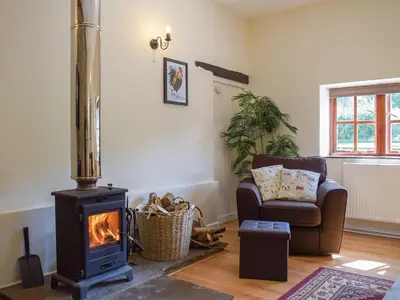 a living room with a wood stove and a chair at Dairy Cottage in Talley