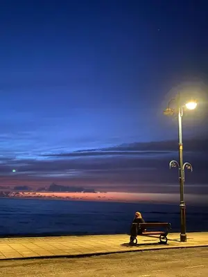 a person sitting on a bench next to a street light at Lovely Seafront 2 bed flat in Aberystwyth in Aberystwyth