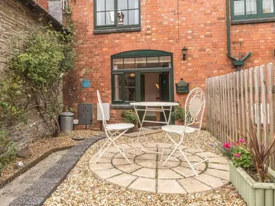 a patio with two chairs and a table in front of a brick building at Stable Cottage, Bishops Castle in Bishops Castle