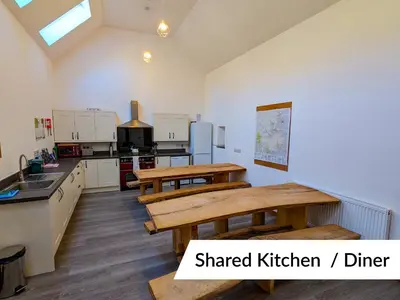 a kitchen with two wooden tables and a kitchen with white cabinets at Cwm Clyd - Carthouse in Rhayader