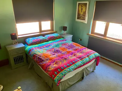 a bedroom with a bed with a colorful comforter and two windows at Mountain Suite, Stunning Views, Brecon Beacons in Llanhamlach