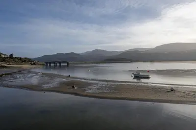 a boat on the shore of a river with a bridge at Harbour View - Flat 2 - Tudor House in Barmouth