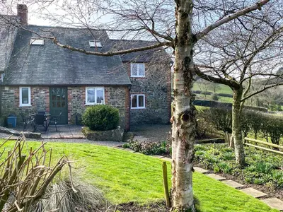 a stone house with a tree in front of it at Heron Cottage in Bishops Castle