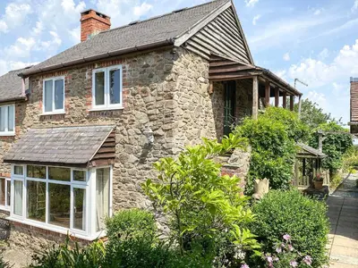 a stone house with white windows and bushes at Curlew Cottage in Bromlow