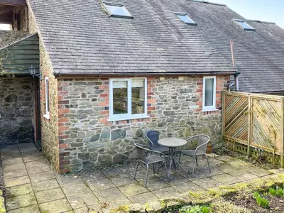 a table and chairs in front of a stone house at Curlew Cottage in Bromlow