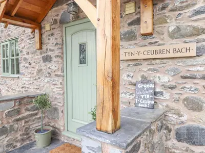 a stone building with a green door and a sign at Tyn Y Ceubren Bach at Evelyns Retreat in Corwen
