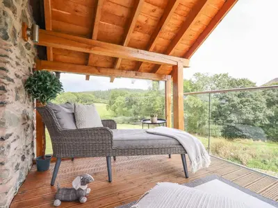 a porch with a wicker chair on a deck at Tyn Y Ceubren Bach at Evelyns Retreat in Corwen