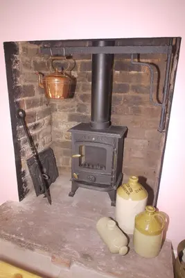 a stone fireplace with a stove in a room at The Gardener's Cottage in Leominster