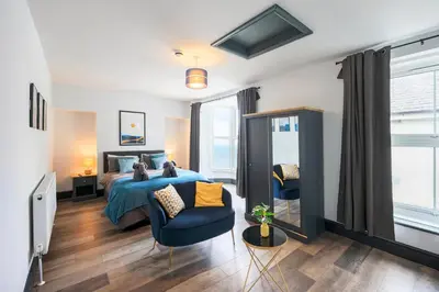 a bedroom with a bed and a blue chair at Seafront apartment with balcony, parking and sea views in Aberystwyth