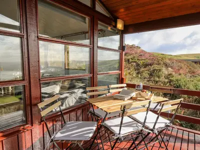 a table and chairs on a balcony with windows at Top Of The World Lodge in Aberdyfi