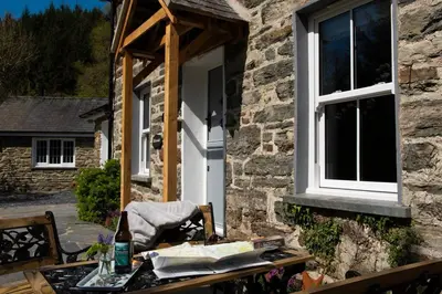 a table in front of a stone house with a window at Charming Riverside Cottage in Snowdonia National Park in Tanygrisiau