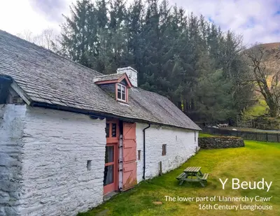 a white barn with a red door and a picnic table at Longhouse - Y Beudy in Rhayader