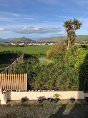 a garden with plants and a fence and a palm tree at Tywyn seaside apartment with Mountain View in Tywyn
