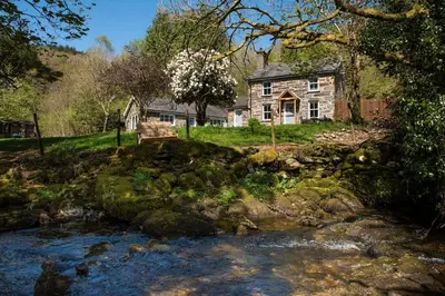 a stone house with a river in front of it at Luxurious Riverside Cottage in Snowdonia National Park in Tanygrisiau