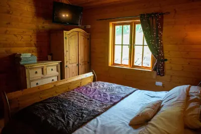 a bedroom with a bed and a dresser and a window at George Cabin - Log Cabin in Wales with Hot tub in Newtown