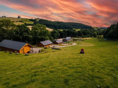 a person is sitting in a field near a house at Bothy Cabin -Log cabin in wales - with hot tub in Newtown
