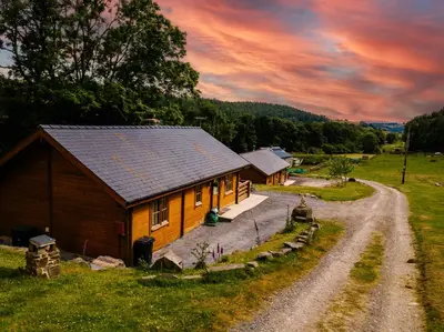 a house in a field with a dirt road next to it at Bothy Cabin -Log cabin in wales - with hot tub in Newtown