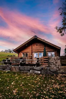 a log cabin in a field with a cloudy sky at Bothy Cabin -Log cabin in wales - with hot tub in Newtown
