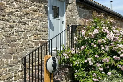 a stone house with a gate and a flower bush at Camlad Barn in Chirbury